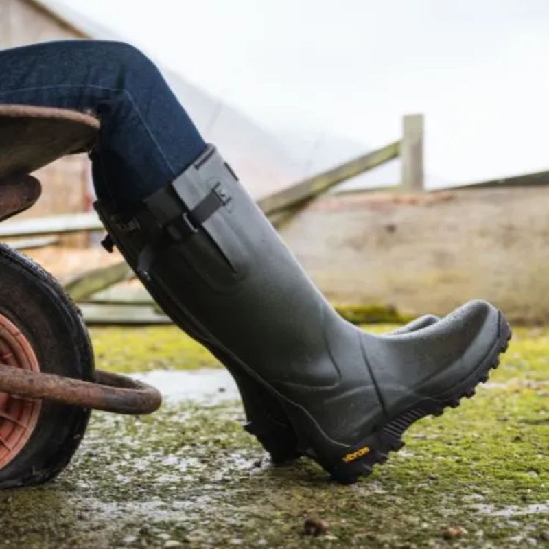 Woman wearing wellington boots on muddy ground using a wheelbarrow